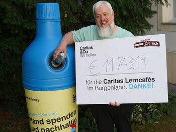 Caritas Direktor Norbert Filipitsch steht mit einem Spendenscheck neben einem Pfandaufsteller in Form einer blauen PET-Flasche.