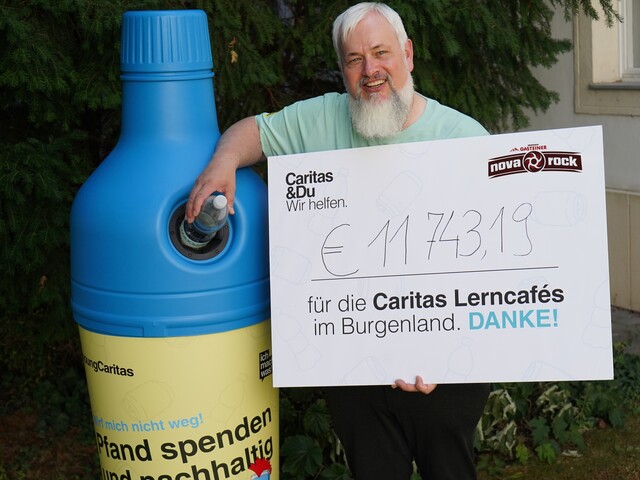 Caritas Direktor Norbert Filipitsch steht mit einem Spendenscheck neben einem Pfandaufsteller in Form einer blauen PET-Flasche.