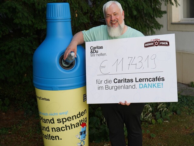 Caritas Direktor Norbert Filipitsch steht mit einem Spendenscheck neben einem Pfandaufsteller in Form einer blauen PET-Flasche.