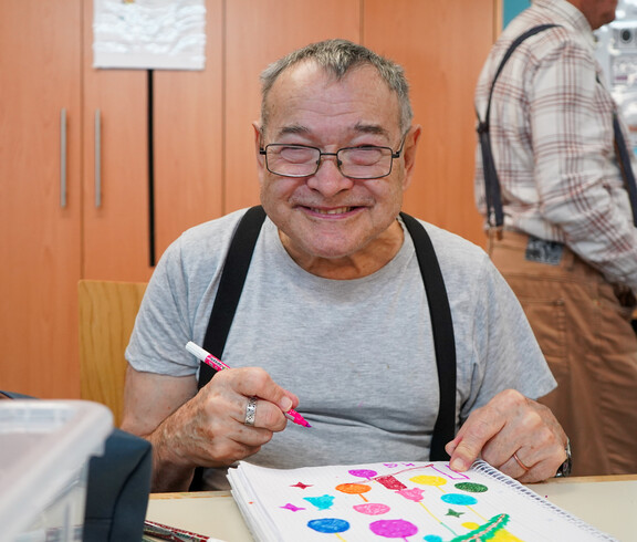 Ein älterer Bewohner lächelt und hält einen Filzstift in der Hand.