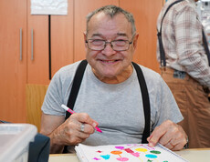 Ein älterer Bewohner lächelt und hält einen Filzstift in der Hand.