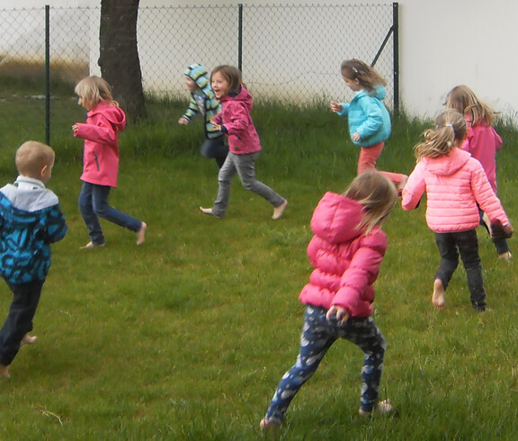 Kinder aus dem Caritas Kindergarten Unterfrauenhaid laufen barfuß im Rasen beim feuchten Tau-Lauf.