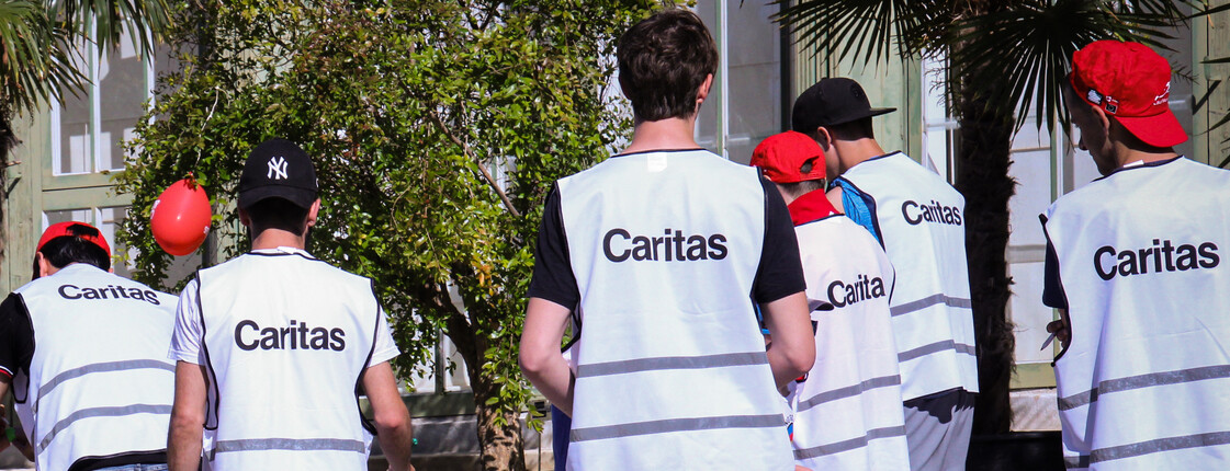 Eine Gruppe von Menschen mit Caritas Weste steht bei zwei Kindern.  