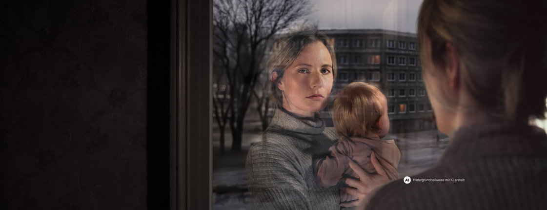 Eine Frau mit Kind am Arm schaut aus dem Fenster. Ihr Gesicht spiegelt sich im Fensterglas wider. Vor dem Fenster ist eine Wohngegend erkennbar.