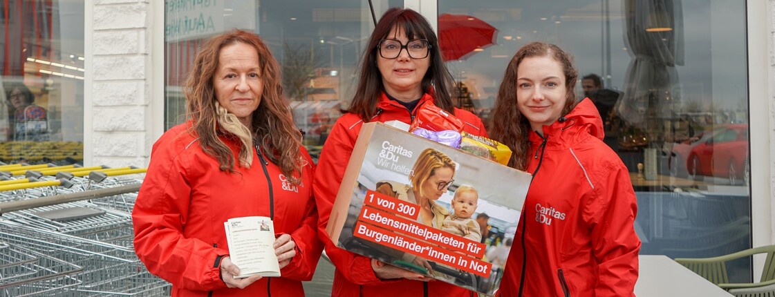 Caritas Direktorin Melanie Balaskovics und zwei Kolleginnen aus dem Bereich Beratung & Hilfe stehen mit einem Lebensmittelpaket vor einer Billa Filiale.