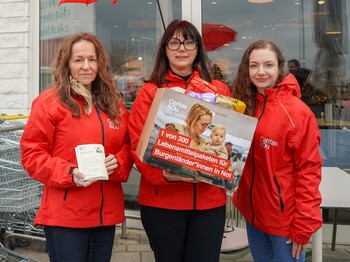 Caritas Direktorin Melanie Balaskovics und zwei Kolleginnen aus dem Bereich Beratung & Hilfe stehen mit einem Lebensmittelpaket vor einer Billa Filiale.