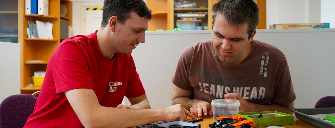 Zwei Männern blicken konzentriert und bauen ein kleines Spielzeugauto.