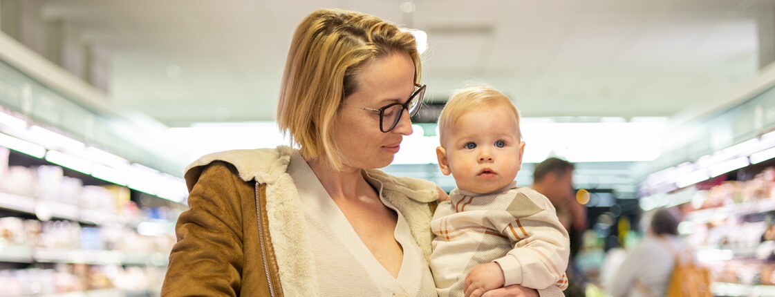 Eine Mutter beim Einkaufen mit einem Kleinkind auf dem Arm.