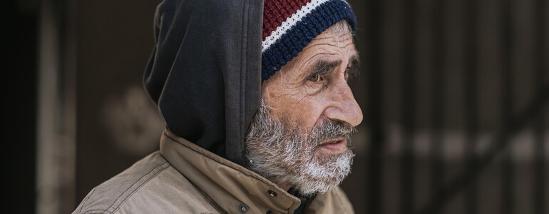 Seitenansicht von einem obdachlosen Mann mit winterlicher Kleidung.