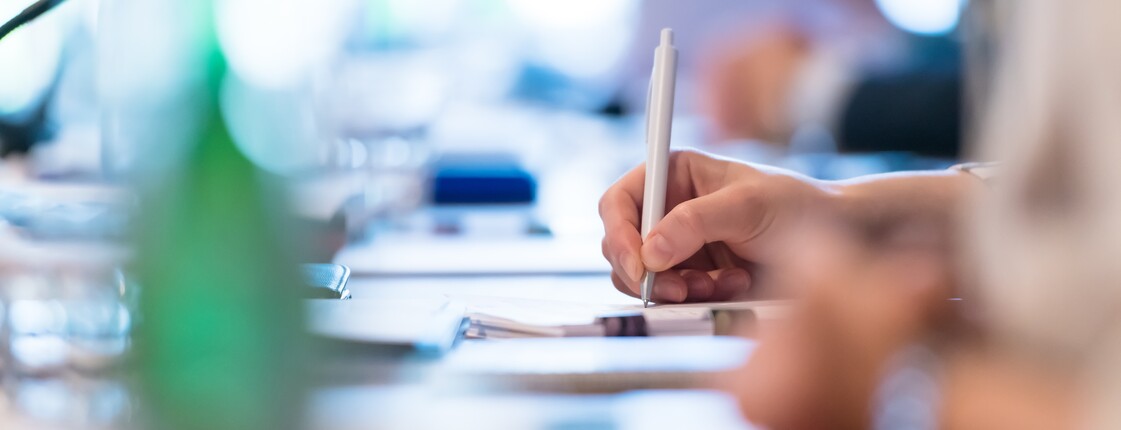 Eine Hand schreibt mit Kugelschreiber etwas auf einen Block.