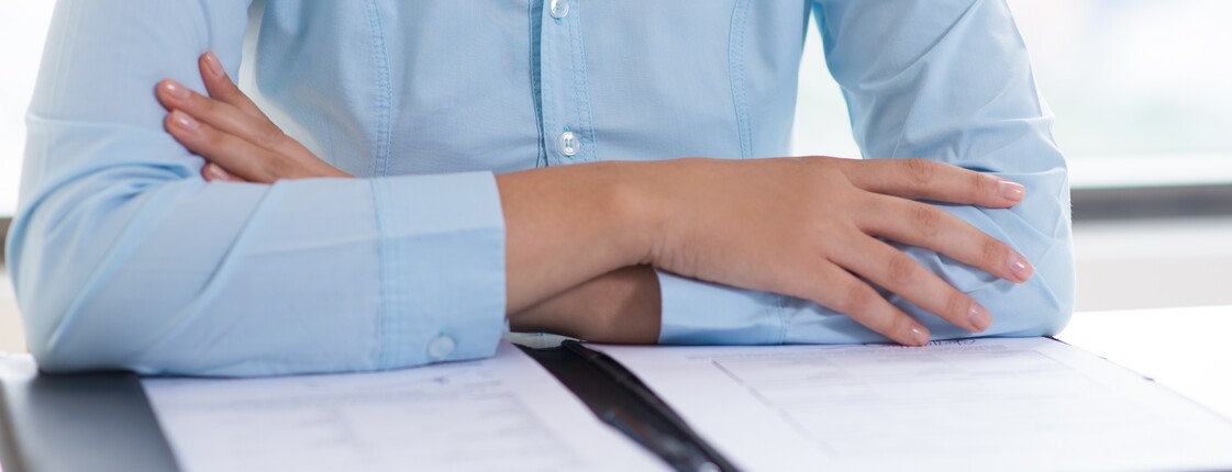 Professionell gekleidete Frau sitzt vor einer Mappe mit Unterlagen.