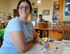 Eine Frau sitzt an einem Tisch und bemalt eine Schablone.