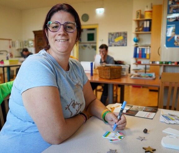 Eine Frau sitzt an einem Tisch und bemalt eine Schablone.