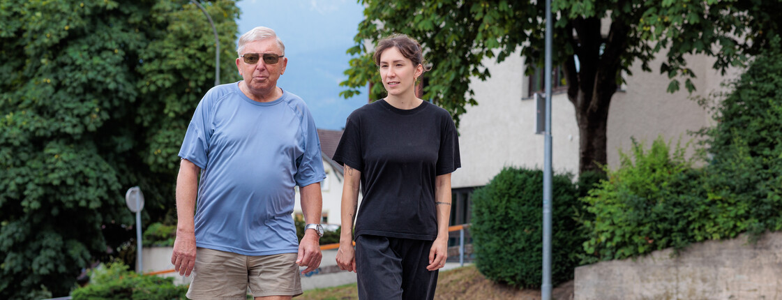 Eine Ehrenamtliche begleitet einen Angehörigen regelmäßig bei Spaziergängen in der Nachbarschaft.