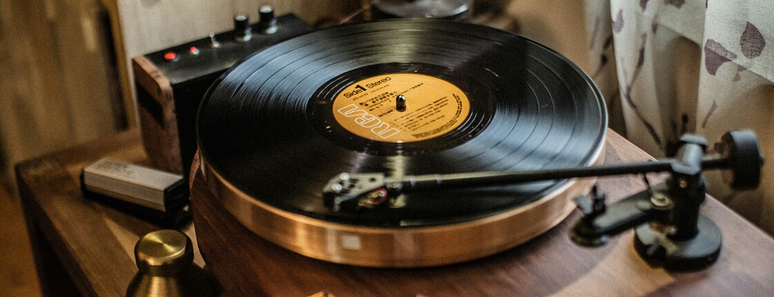 Votr einem Fenster mit Gardine steht ein hochwertiger Plattenspieler aus Holz mit einer alten Schallplatte.