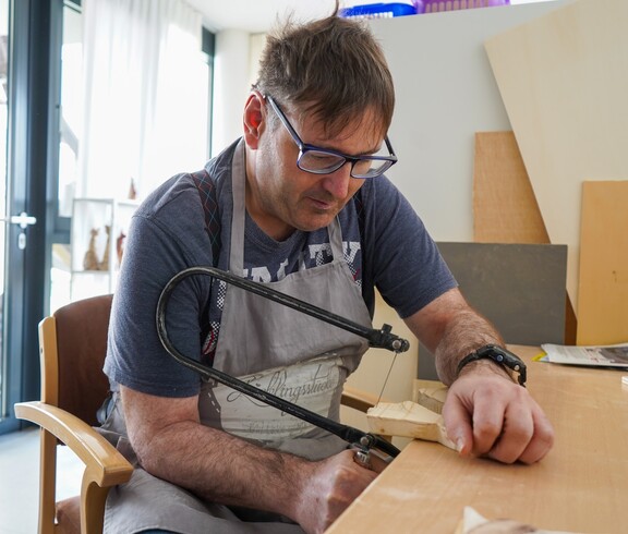Ein Bewohner aus dem Haus Lisa schneidet mit einer Säge ein Stück Holz
