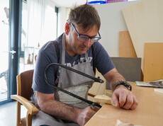 Ein Bewohner aus dem Haus Lisa schneidet mit einer Säge ein Stück Holz