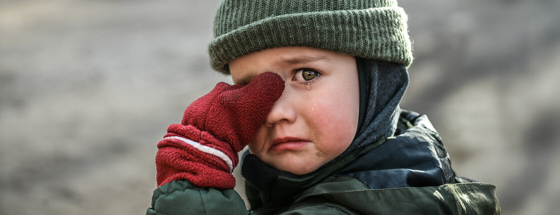Kind mit Mütze und roten Handschuhen wischt sich weinend die Augen ab
