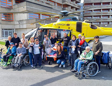 Bewohner*innen und Betreuer*innen des Haus St. Stephan waren am Tag der offenen Klinktür dabei. Sie stehen als Gruppe gemeinsam vor einem gelben Hubschrauber und lächeln in die Kamera.
