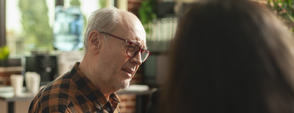Ein älterer Mann sitzt und spricht mit einer Frau.