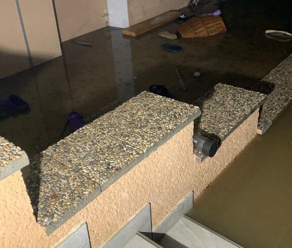 Ein überschwemmter Kellerbereich im Südburgenland, in dem Wasser Gegenstände wie Schuhe und Körbe umspült, während die Treppe ins Wasser führt und die Wände nass sind.