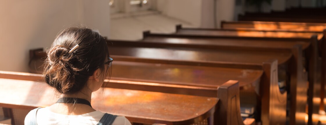 Junge Frau sitzt in der Kirche Eine junge Frau sitzt in der Kirche. Ihr Gesicht ist nicht zu erkennen.
