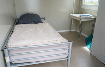 Innenbereich des Containers mit einem Einzelbett und einem kleinen Tisch.