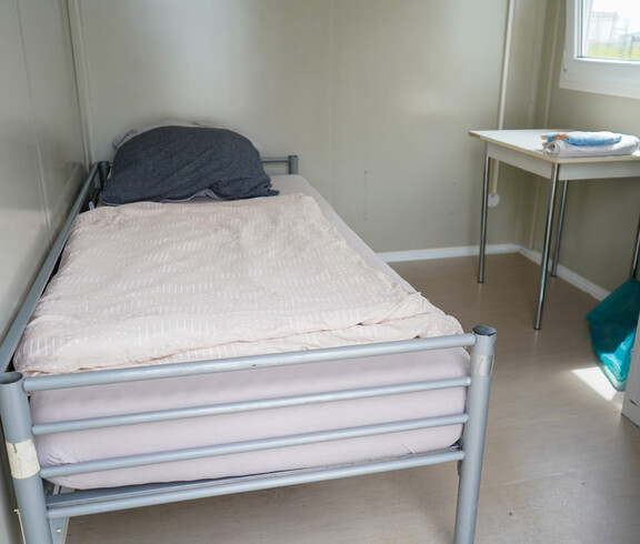 Innenbereich des Containers mit einem Einzelbett und einem kleinen Tisch.