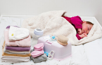 Ein Baby liegt auf einer Decke, daneben Windeln, Hygieneartikel und Kleidung.