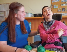Eine Bewohnerin aus dem Behindertenbereich und eine Betreuerin sitzen lachend an einem Tisch und spielen