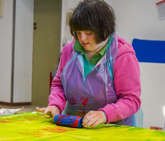 Eine Frau malt mithilfe einer Farbrolle auf einer gelben Leinwand.