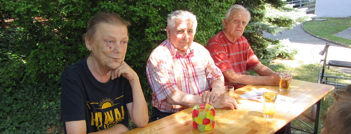 Im Schatten genießen die Herren Spritzer und Gegrilltes im Caritas Haus Elisabeth in Rechnitz