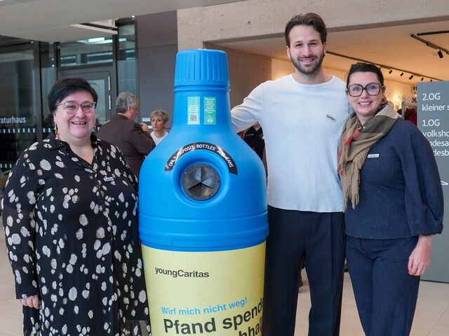 Caritas Burgenland Direktorin Melanie Balaskovics und zwei Mitarbeiter*innen stehen neben einem Pfandaufsteller.
