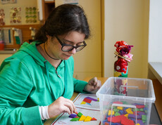 Eine junge Frau sitz an einem Tisch und macht ein Puzzle mit bunten Steinen.