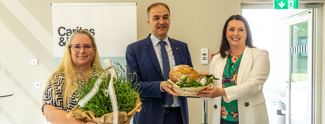 Zwei Frauen und ein Mann mit Blumenstrauß und Brot