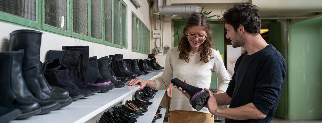 Ein Mann und eine Frau stehen in einem Second-Hand-Shop vor Regalen mit schwarzen Schuhen und sortieren gemeinsam Schuhe aus.