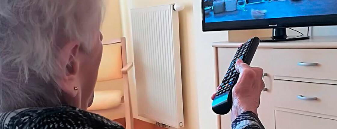 Alte Frau sitzt vor Fernseher mit Fernbedienung in der Hand