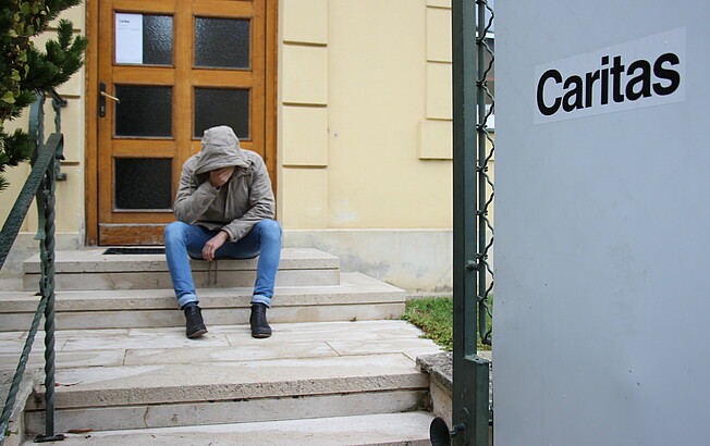 Mann sitzt verzweifelt auf Stiegen vor der Caritas Sozialberatung
