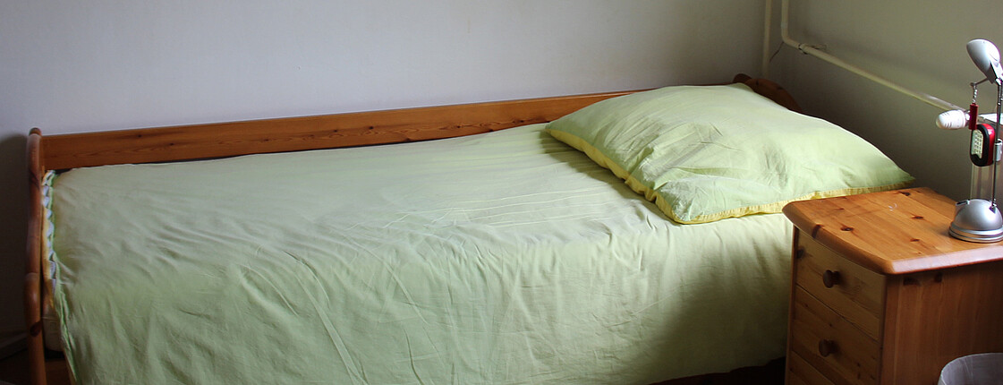 Ein Bett mit Nachtkästchen in der Caritas Notschlafstelle