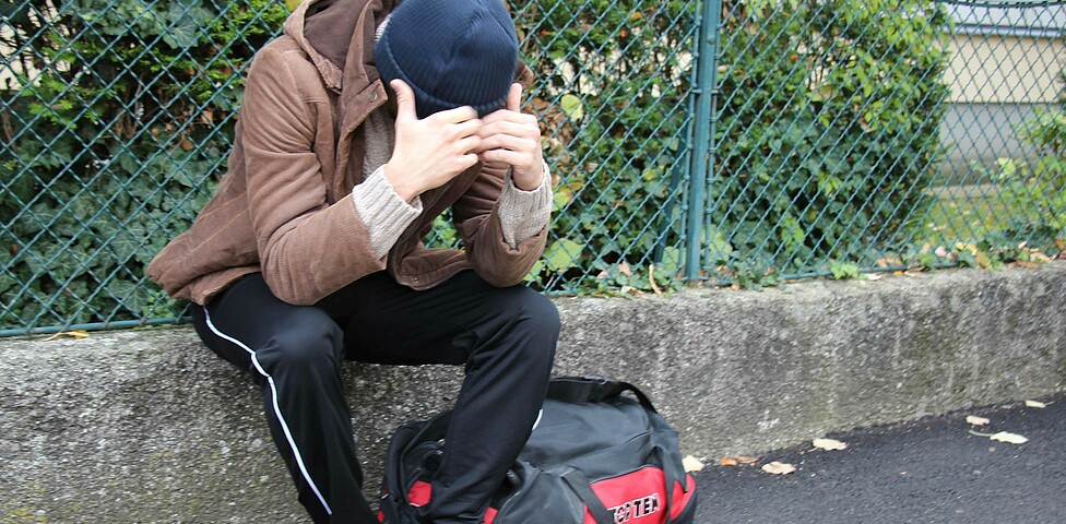 Obdachloser Jugendlicher sitzt verzweifelt auf der Straße mit einer großen Taschen