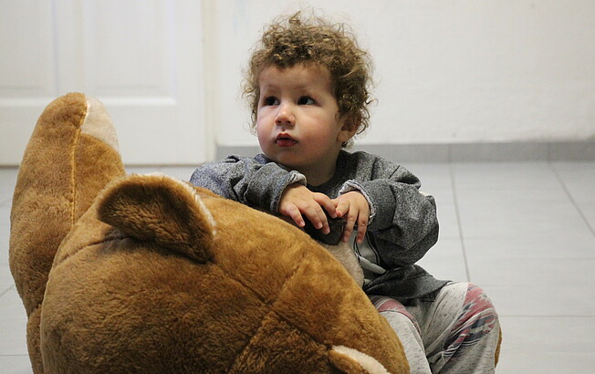 Ein kleiner Bub im Mutter-Kind-Haus spielt mit einem Teddy.