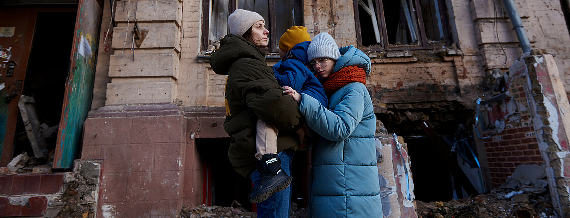 Frau mit Kindern steht vor zerstörtem Haus in Kiew Ukraine