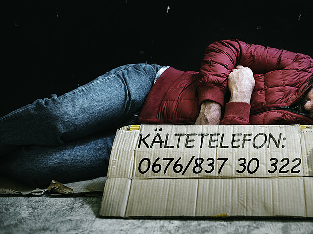 Odachloser auf der Straße mit Telefonnummer vom Kältetelefon der Caritas.